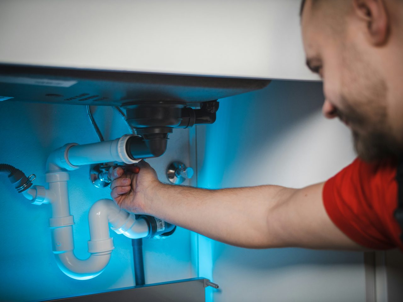Plumber working under a kitchen sink to repair the drain trap and shutoff valves.