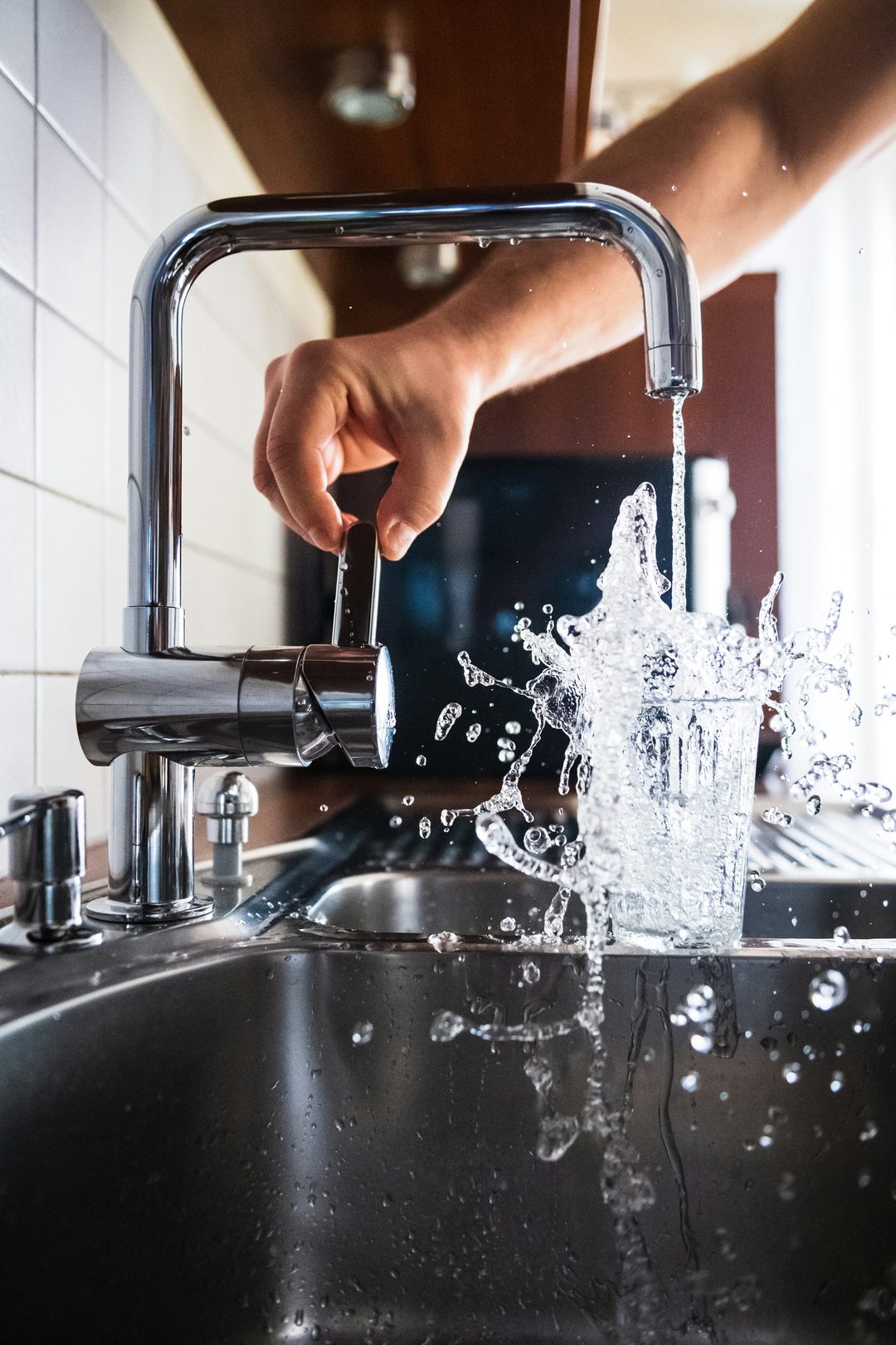 Clear water running from a kitchen faucet into a glass over a stainless steel sink.